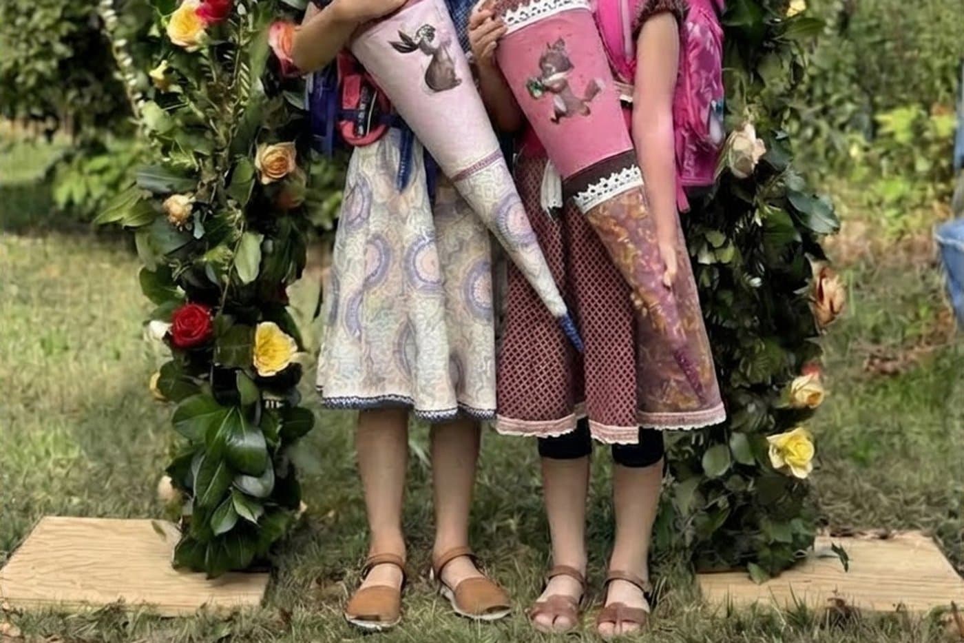 Zwei Kinder mit Schultüten und Ranzen unter einem Rosenbogen am Tag der Einschulung